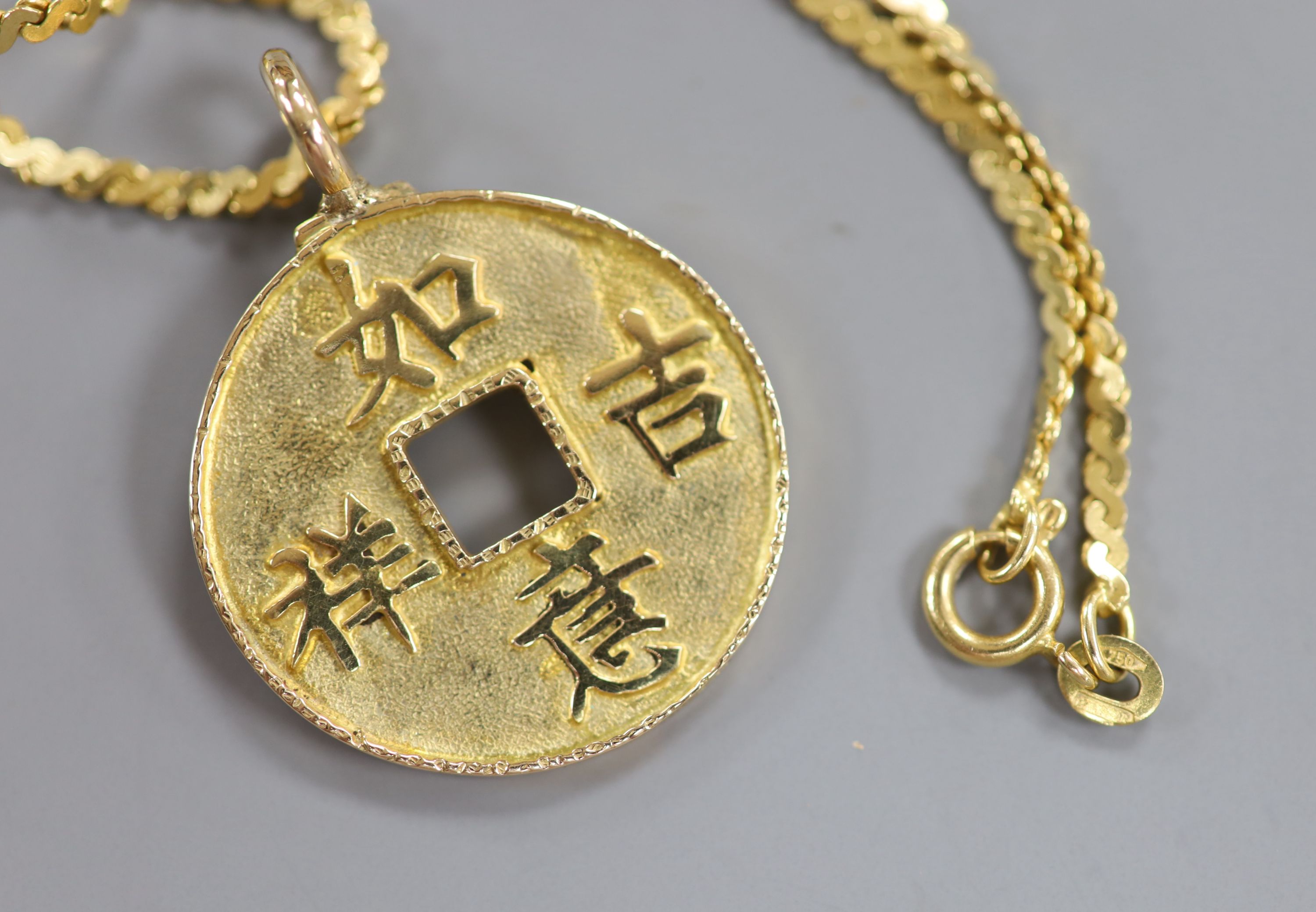 A Chinese yellow metal amulet, on an Italian Uno-A-Erre 750 chain, gross 13 grams.